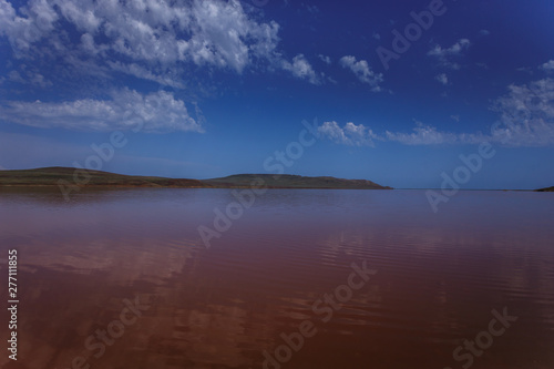The surface of the pink lake and its shore in the background. Incredible clouds are reflected in the water.