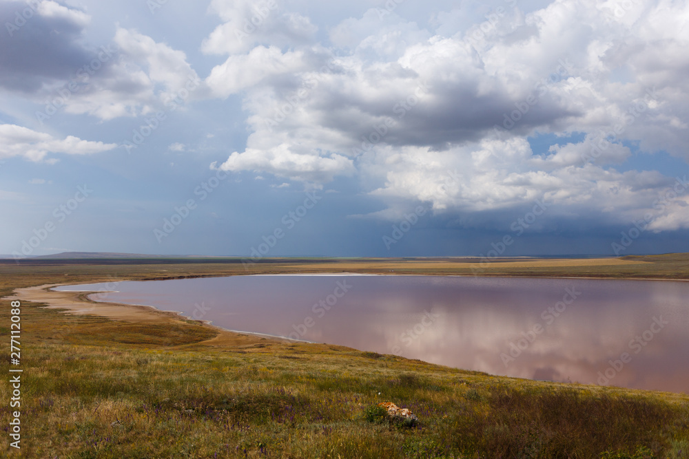 Pink Lake. Clouds are reflected in the water. Nebula-shaped clouds are floating across the sky. Summer sunny day.