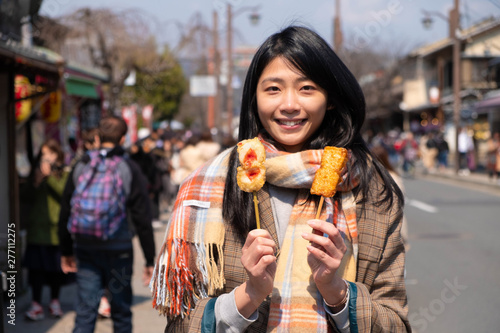 Young woman's hands holding two sticks of japanese fried snack. Happy tourist enjoying local food in Japan. Popular street food along arashiyama, Kyoto, Japan.