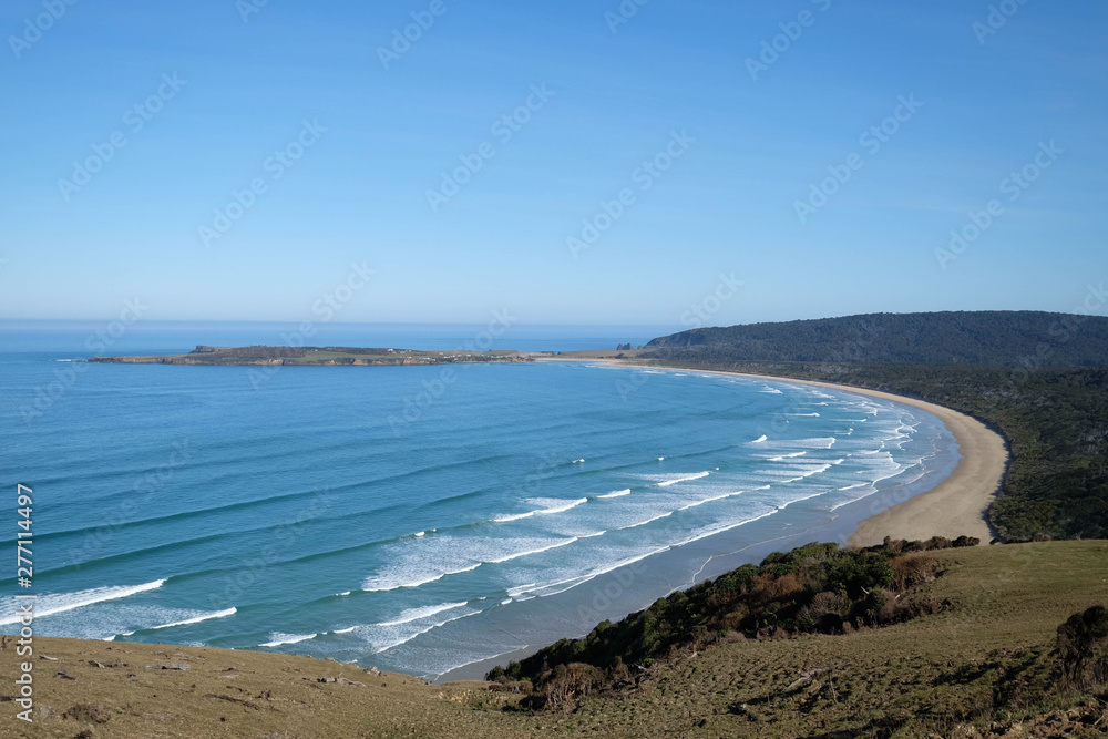 A lookout of a beautiful beach in New Zealand. There are blue sky, clear water and sandy beach. This is a great place for relaxation and recreation activities. It is popular among travelers.