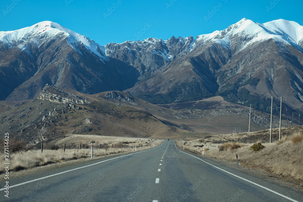 A long straight road leading towards a snow capped mountain in New Zealand.
