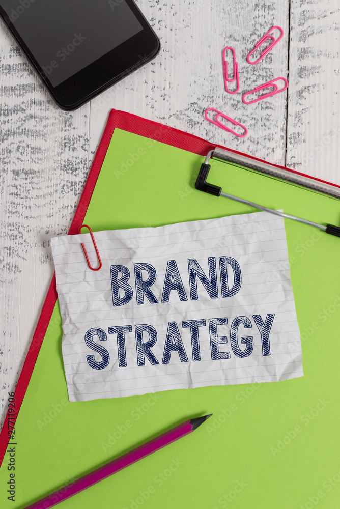 Handwriting text Brand Strategy. Conceptual photo Long term marketing support for a product Marketing Clipboard paper sheet pencil smartphone note clips wooden retro background Handwriting text Brand Strategy. Conceptual photo Long term marketing support for a product Marketing Clipboard paper sheet pencil smartphone note clips wooden retro background