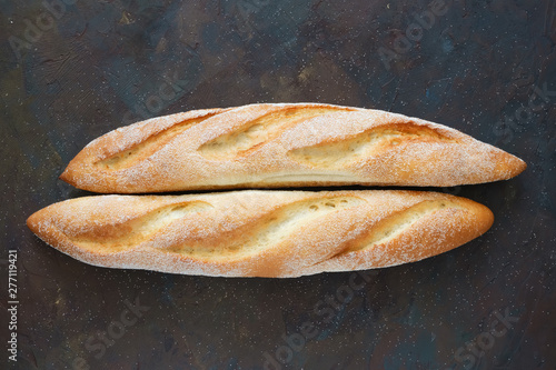 Two freshly baked baguettes on dark brown background. Top view.