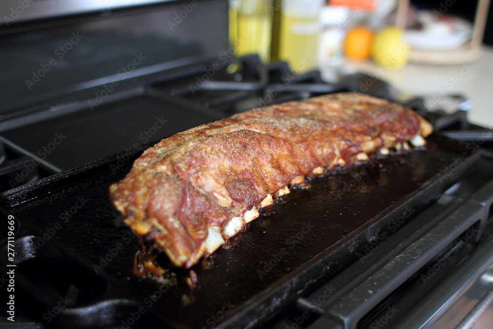 Rack of dry rub pork ribs baked on a cast iron tray, resting on the stove top.