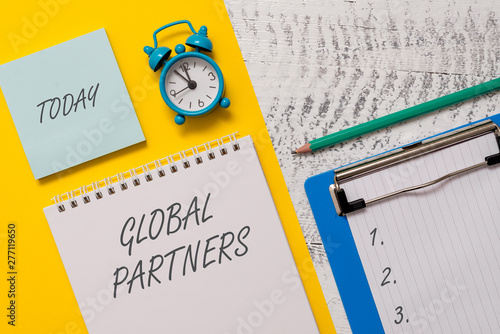 Conceptual hand writing showing Global Partners. Concept meaning Two or more firms from different countries work as a team Spiral notepad sheet marker alarm clock wooden background photo