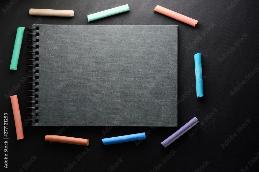 Bright multi-colored chalk on a black background. Sketchbook for drawing pencils or chalk lies on a dark background Bright multi-colored chalk on a black background. Sketchbook for drawing pencils or chalk lies on a dark background