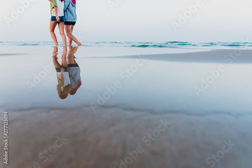 Two girls walk along the shore of the beach at sunset.
