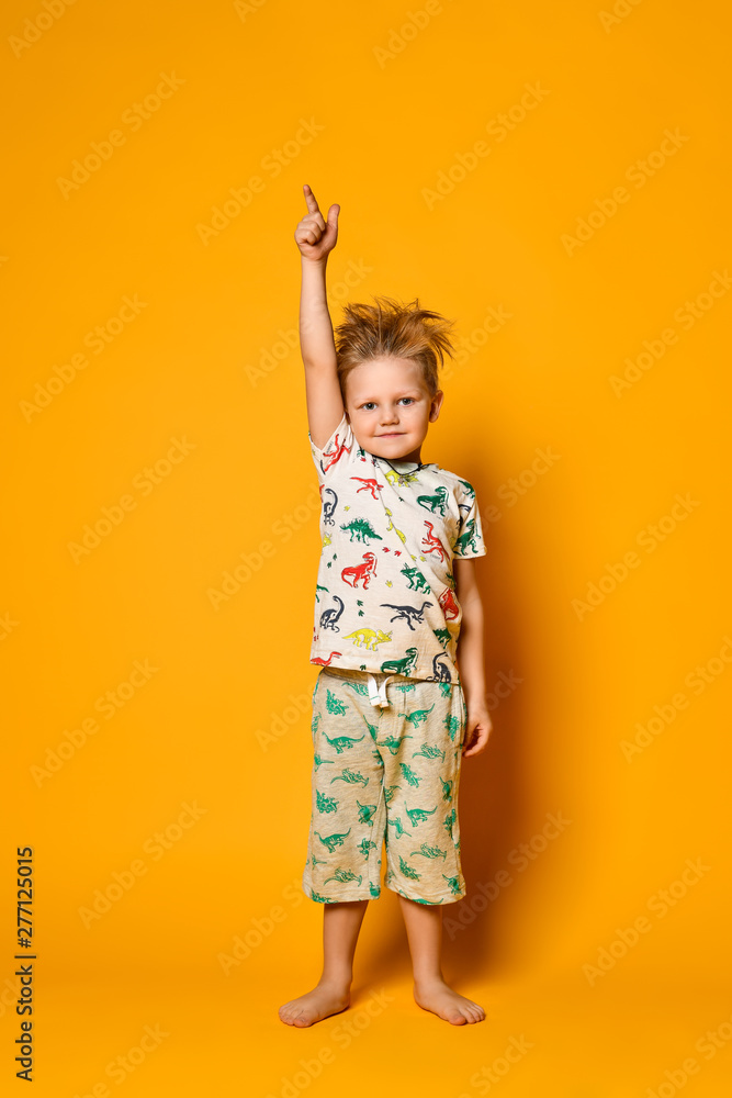 Little cute blond boy preschooler in pajamas with dinosaurs having fun has joy in the studio over yellow background. Little cute blond boy preschooler in pajamas with dinosaurs having fun has joy in the studio over yellow background.