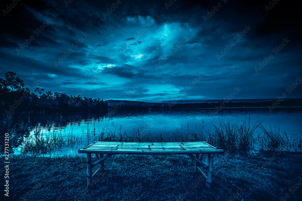 bamboo litter on grass in front of lake and moonlight behind a cloudy at night time