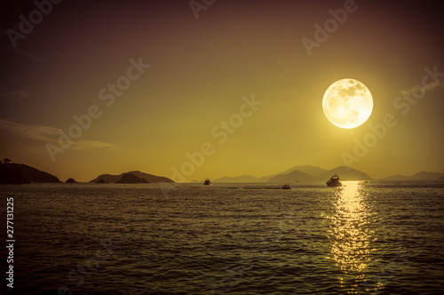 Scenic view of small boat in calm sea water at night time and super moon.