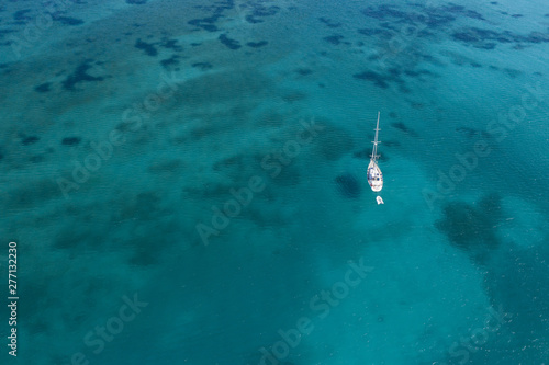 View from above, stunning aerial view of a yacht sailing on a beautiful turquoise clear water. Spiaggia La Pelosa (Pelosa beach) Stintino, Sardinia, Italy.