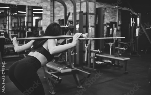 Slim brunette athlete doing gymnastic exercise with body bar on her shoulders tilting her body in the gym. Back view