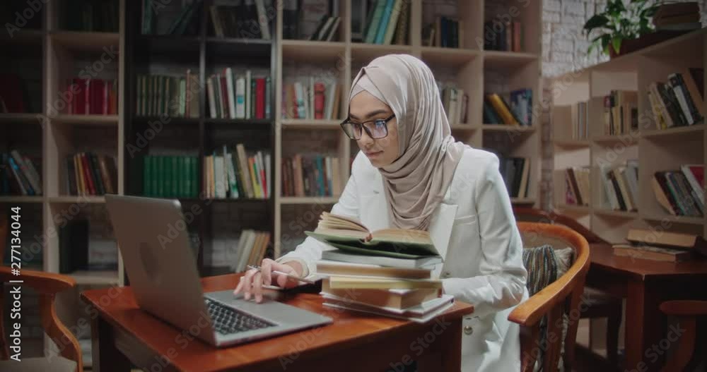 Female muslim student is studying at desk in library, using laptop and books. Girl wearing hijab is preparing for exams - student lifestyle, modern islam concept 4k close up Female muslim student is studying at desk in library, using laptop and books. Girl wearing hijab is preparing for exams - student lifestyle, modern islam concept 4k close up