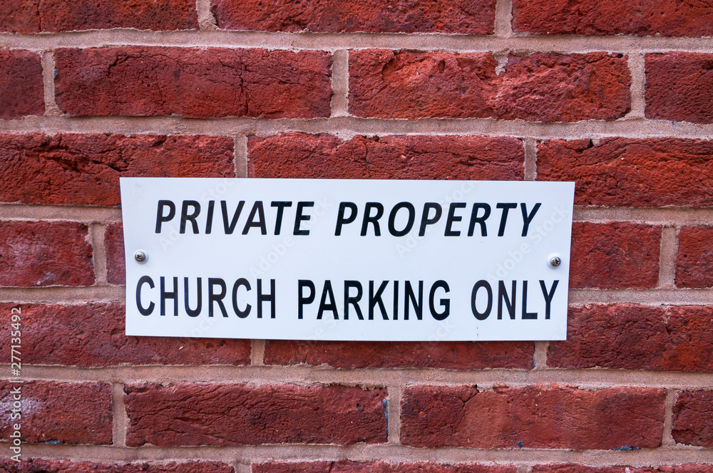 A white metal sign that says PRIVATE PROPERTY CHURCH PARKING ONLY on a brick wall A white metal sign that says PRIVATE PROPERTY CHURCH PARKING ONLY on a brick wall