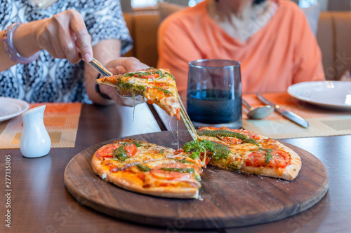 Woman hand picking a piece of pizza on wooden board in restaurant.