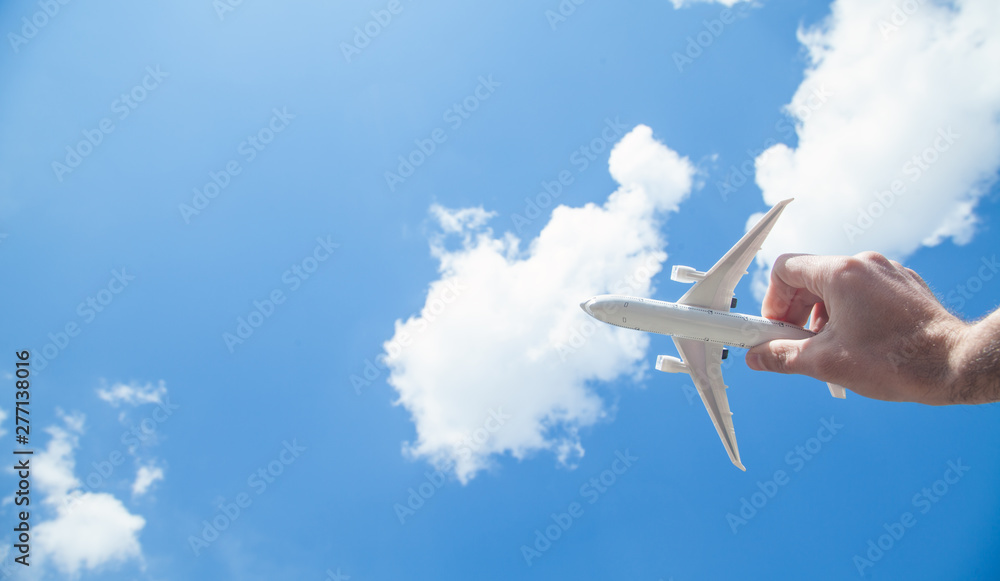Hand holding airplane model in front of blue sky background. Travel - obrazy, fototapety, plakaty 