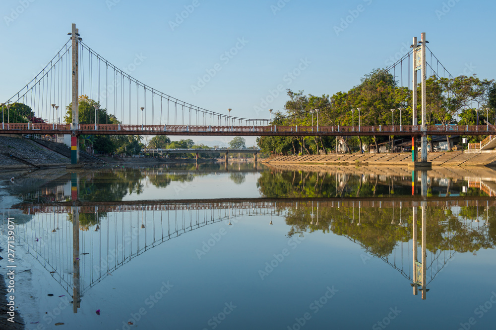 Obraz premium Beautiful scenery view of the iconic suspension bridge (other name is orange bridge) crossing above the Wang river in Lampang downtown, Lampang province of Thailand.