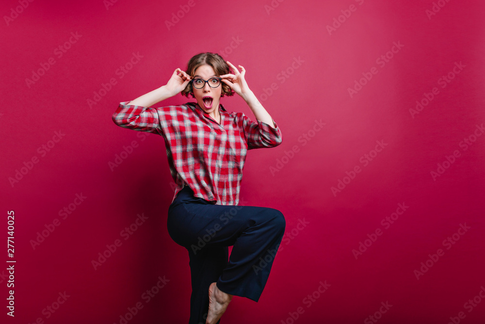 Fascinating girl in black pants dancing and making funny faces. Indoor portrait of fashionable lady in glasses posing on claret background. Fascinating girl in black pants dancing and making funny faces. Indoor portrait of fashionable lady in glasses posing on claret background.