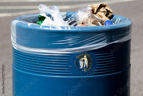 Canvas Print Overflowing blue metal public waste bin with plastic liner