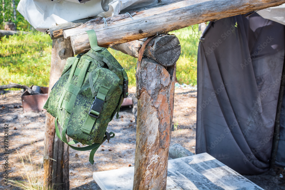 Fototapeta premium Hiking backpack hangs on wooden stick at place to relax in summer forest.