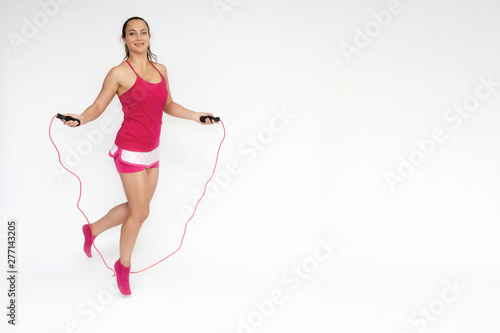Full-length portrait on white background of beautiful pretty fitness girl woman in pink sport uniform standing exercises in different poses with a skipping rope. Smiles Stylish trendy youth.