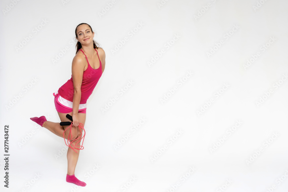 Full-length portrait on white background of beautiful pretty fitness girl woman in pink sport uniform standing exercises in different poses with a skipping rope. Smiles Stylish trendy youth. Full-length portrait on white background of beautiful pretty fitness girl woman in pink sport uniform standing exercises in different poses with a skipping rope. Smiles Stylish trendy youth.