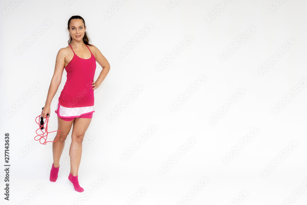 Full-length portrait on white background of beautiful pretty fitness girl woman in pink sport uniform standing exercises in different poses with a skipping rope. Smiles Stylish trendy youth. Full-length portrait on white background of beautiful pretty fitness girl woman in pink sport uniform standing exercises in different poses with a skipping rope. Smiles Stylish trendy youth.