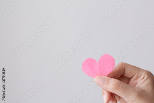 Female hand holding pink paper heart shape with copy space.  