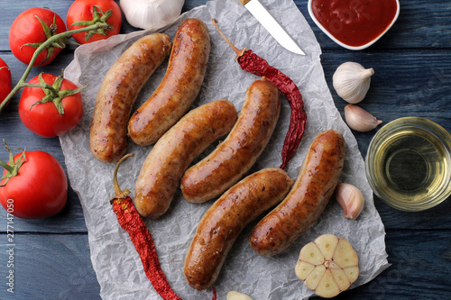 Delicious grilled sausages on paper with red sauce and spices on blue wooden background. B-B-Q. top view