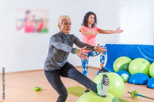 Group of active cheerful sporty women doing single leg squats with balance ball training indoors in gym photo