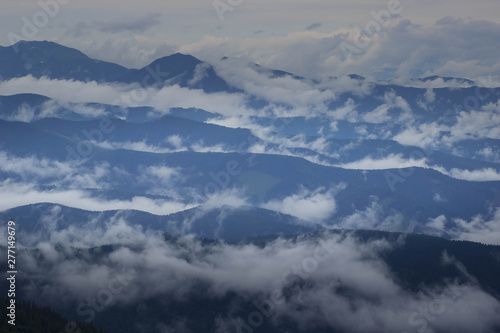 Mountain range with visible silhouettes through the morning colorful fog. © Shcherbyna