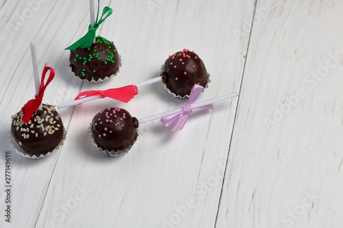Cake pops decorated with a bow of braid. They lie on the boards, painted white.