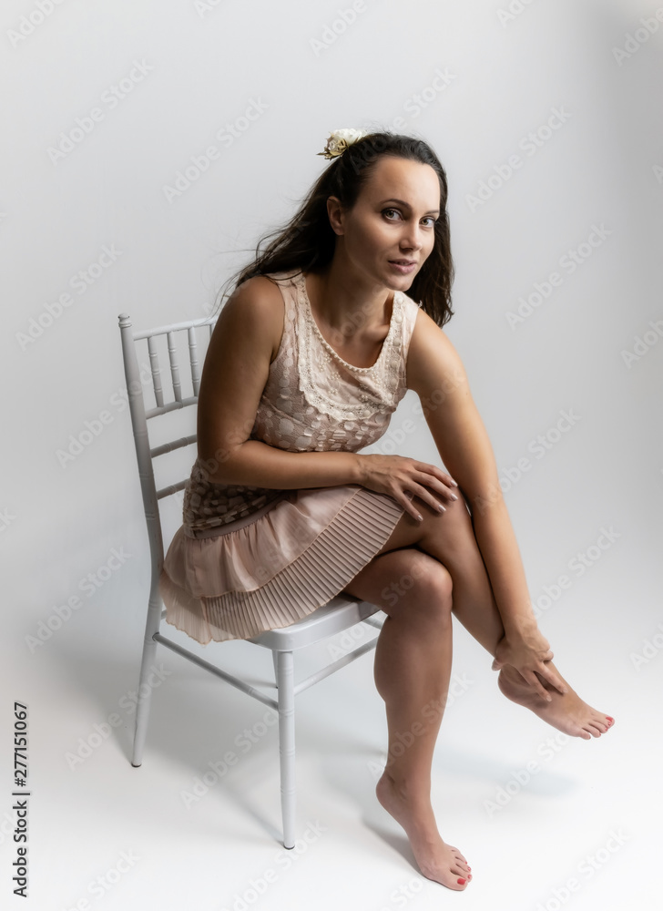 Horizontal portrait full length sitting on a white chair on a white background beautiful pretty woman in a fashionable light pink dress, in various poses. Stylish trendy youth.