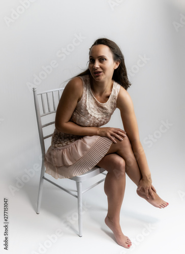 Horizontal portrait full length sitting on a white chair on a white background beautiful pretty woman in a fashionable light pink dress, in various poses. Stylish trendy youth. © Вячеслав Чичаев