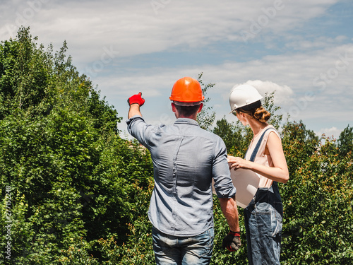 Young engineer woman and her subordinate worker holding a paper project in the park against the backdrop of green trees. Close-up. Concept of labor and employment