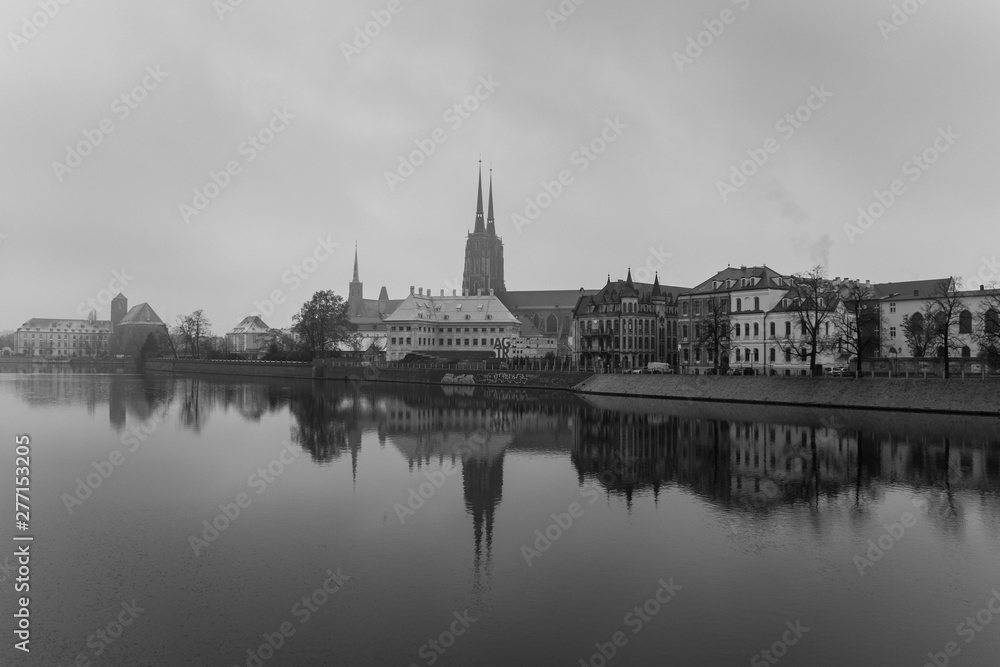 Black and white view of the Cathedral of St. John the Baptist reflected in Oder river at cold snowy day. Ostrow Tumski district. Wroclaw. Poland