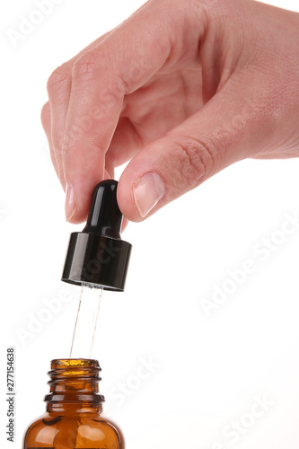 Cosmetic pipette in the hand on white background. Essential oil falling from glass dropper
