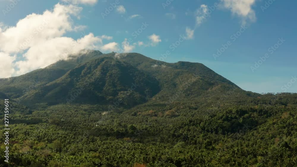 Mountains covered rainforest, trees and blue sky with clouds, aerial view. Camiguin, Philippines. Mountain landscape on tropical island with mountain peaks covered with forest. Slopes of mountains Mountains covered rainforest, trees and blue sky with clouds, aerial view. Camiguin, Philippines. Mountain landscape on tropical island with mountain peaks covered with forest. Slopes of mountains