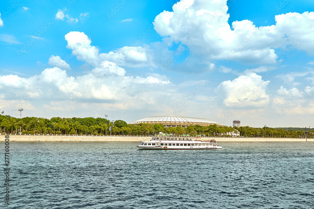 A modern riverboat floats against the backdrop of the city panorama, modern parks. Picturesque modern urban architecture. Tourism, rest in the city, river transport.
