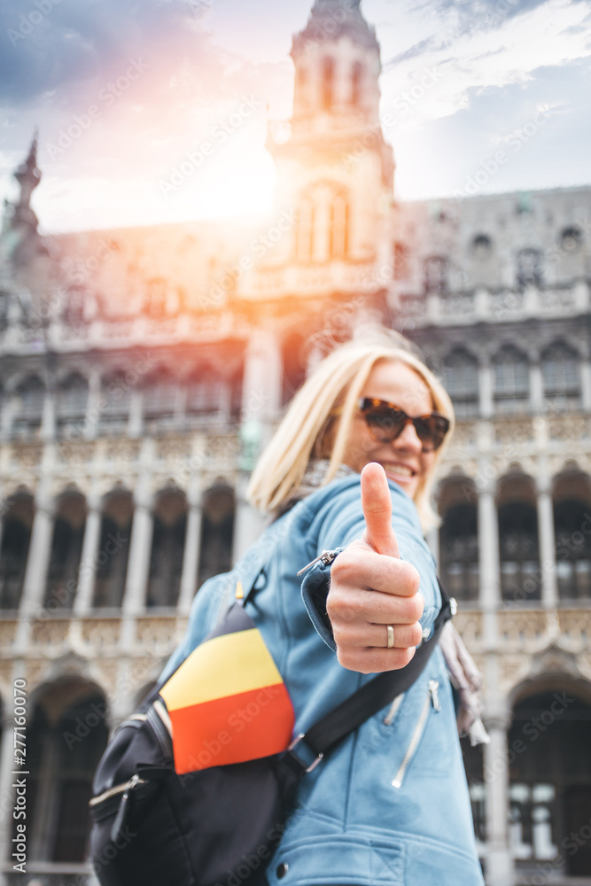 Fototapeta premium A female traveler stands on Grand Place Square in Brussels and shows her thumbs up, Belgium.
