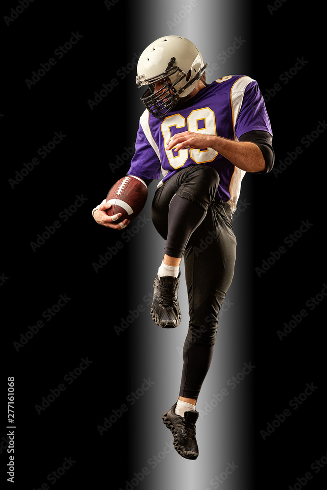 American football player holding a ball while jumping away from a strike. Black background, copy space. Violet with white sportswear.