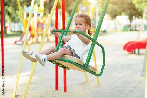 Little Caucasian girl child riding on a swing on the playground on a sunny summer day
