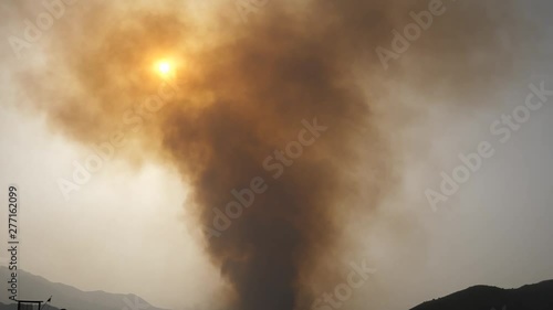 Smoke from a large fire billows into the sky as the sun sets, beach