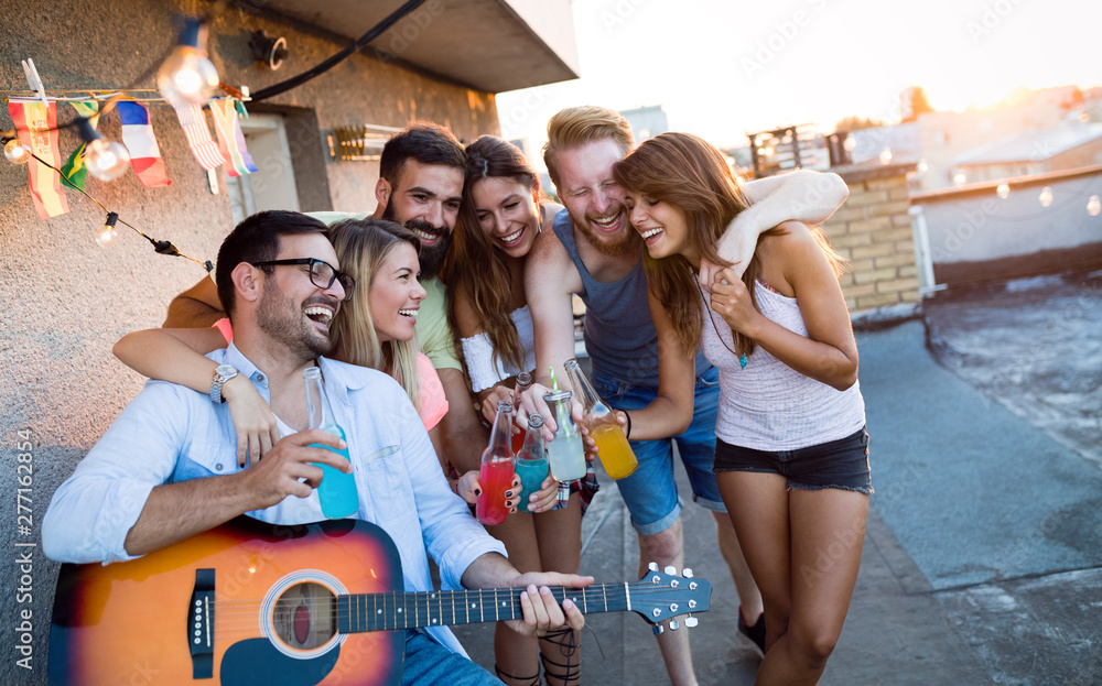 Obraz premium Young friends having fun at a rooftop party, playing the guitar, singing, dancing and drinking