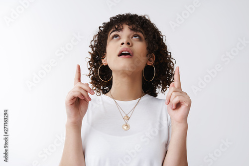Something awesome up there. Amused wondered good-looking curious curly-haired tomboy girl drop jaw open mouth intrigued raise head stare sky upwards pointing index finger interesting promo