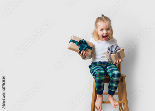 Scandinavian minimalism christmas and new year concept with kid - little girl with stack of gift box on a chair in room