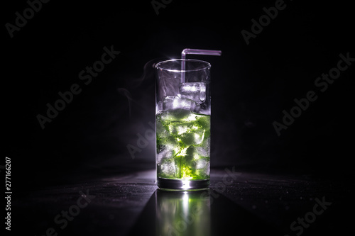 Cocktail glass splashing on dark toned smoky background or colorful cocktail in glass. Party club entertainment. Mixed light.