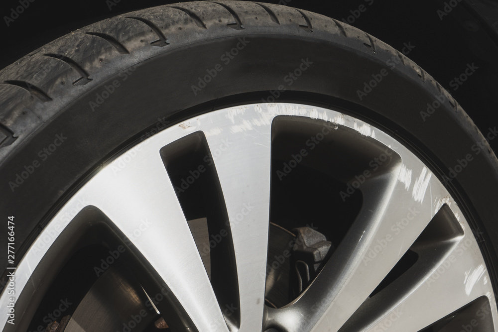 Car wheel closeup. Damaged alloy rim with black thin tire. Bad driver concept. Sunny day.