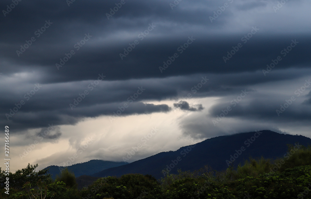 Scenery of black thunderstorm cloudy sky with forest and mountains.