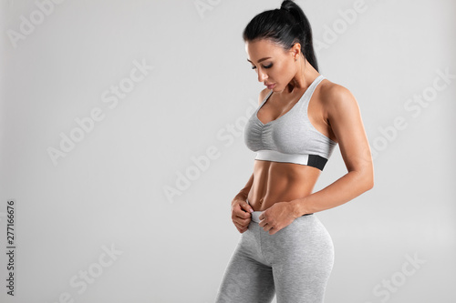 Fitness woman showing abs and flat belly, isolated on gray background. Beautiful athletic girl, shaped abdominal photo